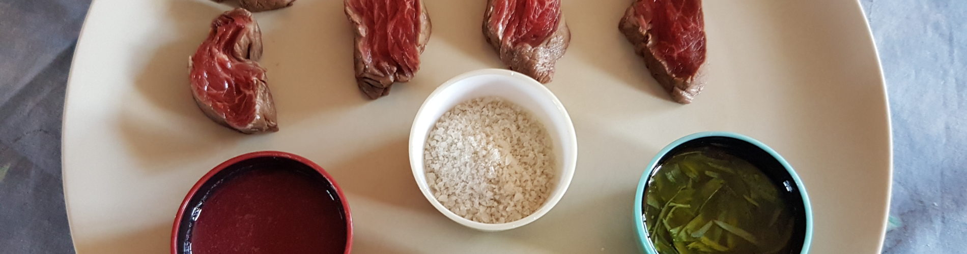 morceaux de viande de boeuf avec trois coupelles de condiments une coupelle de sel