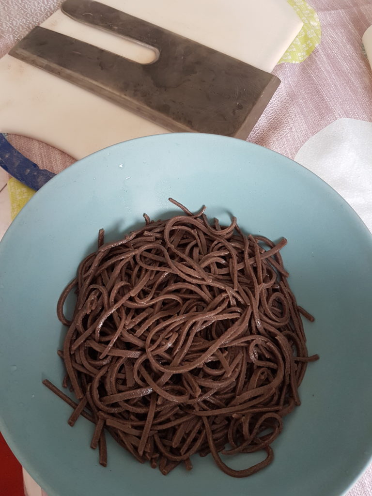 saladier contenant des nouilles de blé noir couteau a nouilles soba en arrière plan