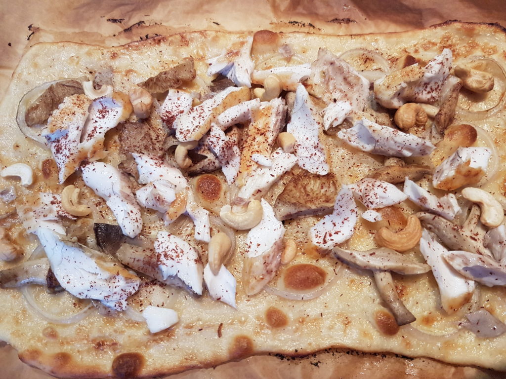 Flammekueche cuite garnie de morceaux de poisson et de champignon avec des noix de cajou