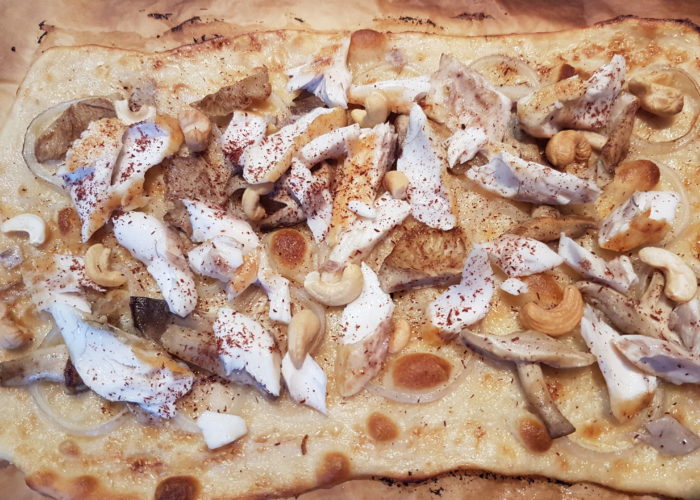 Flammekueche cuite garnie de morceaux de poisson et de champignon avec des noix de cajou