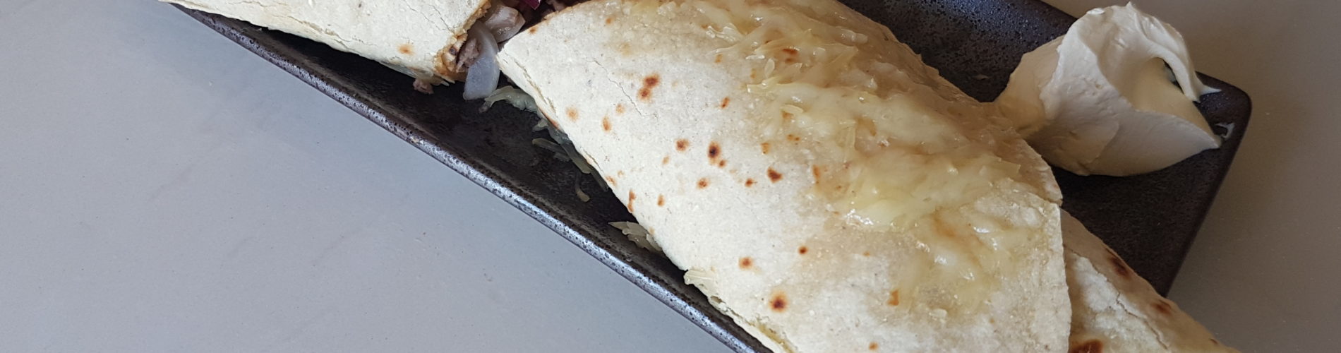 Tortilla remplie et gratinée sur une assiete en cermaique marron rectangulaire avec des sauces dans les deux angles supérieurs