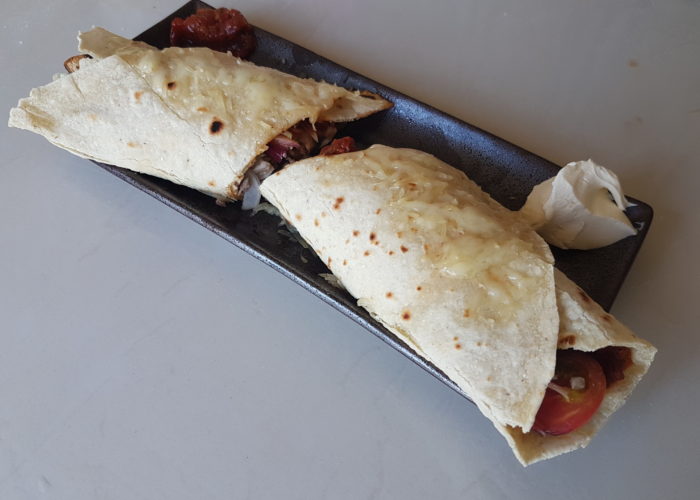 Tortilla remplie et gratinée sur une assiete en cermaique marron rectangulaire avec des sauces dans les deux angles supérieurs