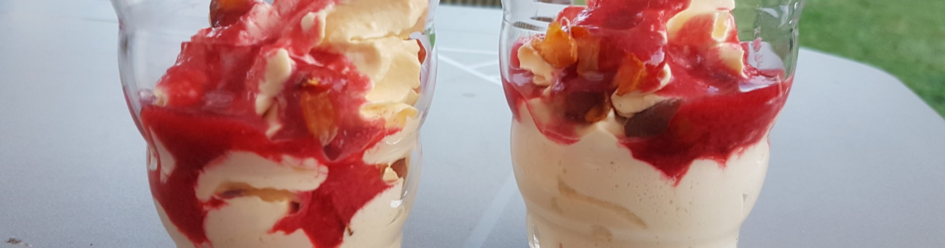 deux verres fantaisie sans dessin contenant une mousse blanchatre légèrement orangée avec de petits morceaux de fruit orange et du coulis de fruit rouge