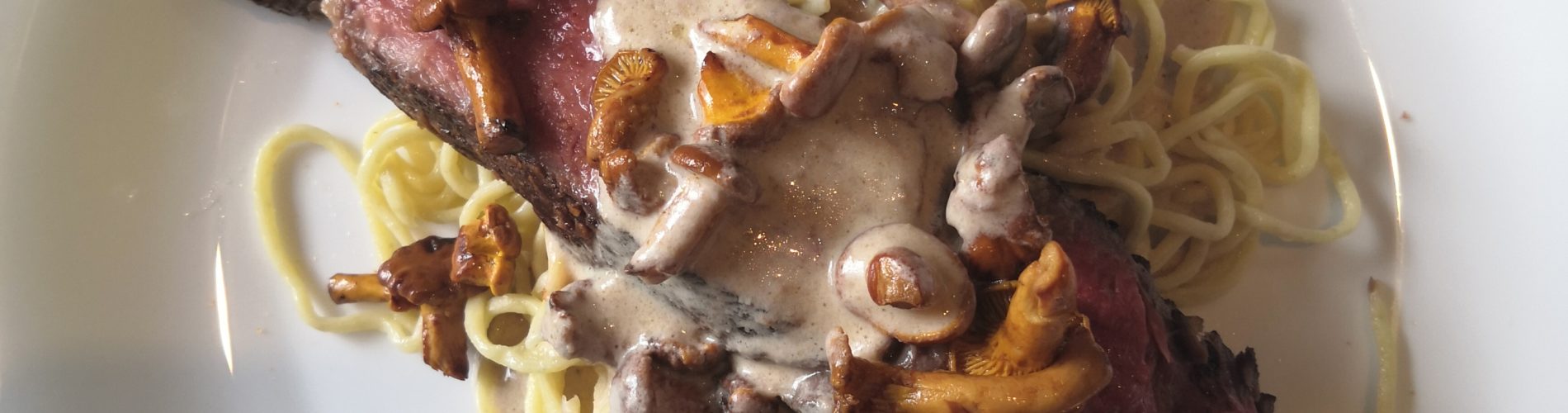 piece de boeuf cuite, spaghetti et champignons sur une assiette blanche