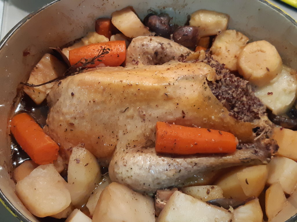 pintade cuite entourée de légumes dans une cocotte en fonte