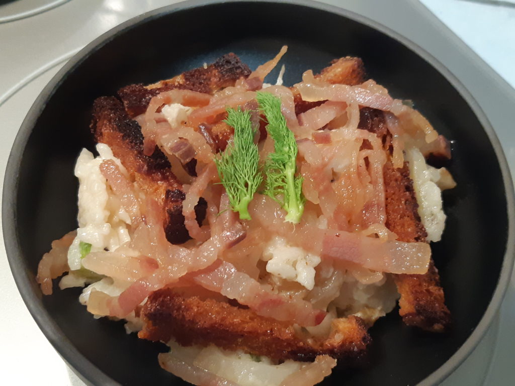 Risotto garni dans un bol noir croutons et lardons visibles avec une pousse de fenouil tout en haut