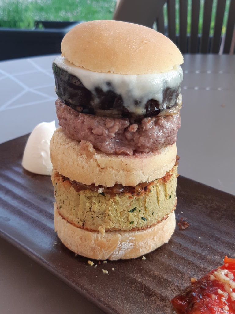 hamburger vertical en gros plan bun, falafel, une fine couche visible de confiture d'oignon, bun, une épaisseur similaire à celle d'un bun de viande hachée claire, un tranche d'aubergine large, de la mozzarelle fondue, bun