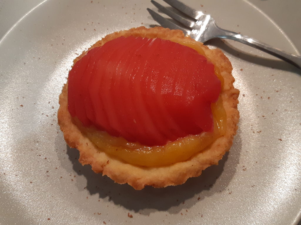 tartelette sur une assiette contenant du fruit en tranche rouge translucide sur une crème jaune