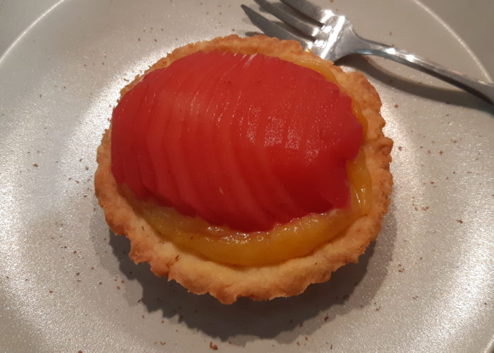 tartelette sur une assiette contenant du fruit en tranche rouge translucide sur une crème jaune