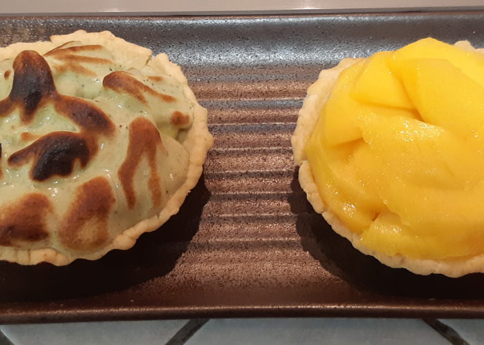 deux tartelettes sur une assiette rectangulaire sombre une avec une meringue verte legerement brulee, l'autre avec des tranches de mangue