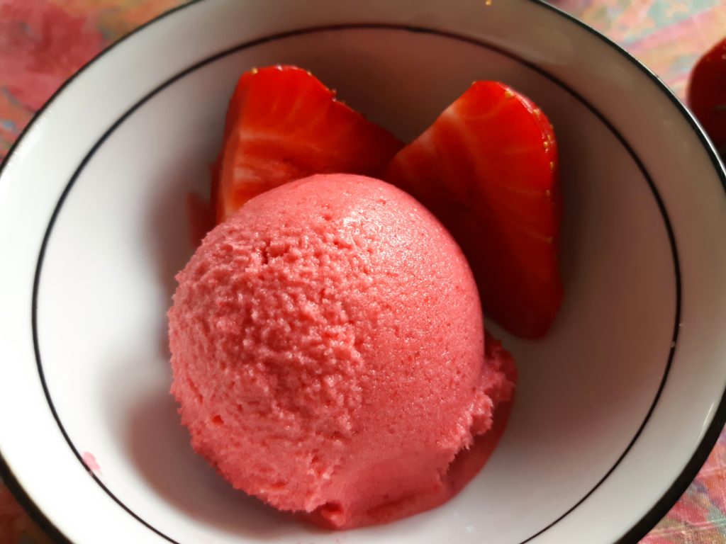 boule de sorbet rose dans un jatte avec deux quartiers de fraise