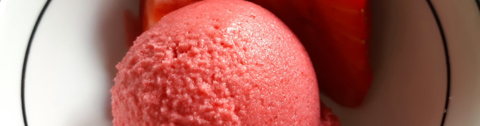 boule de sorbet rose dans un jatte avec deux quartiers de fraise