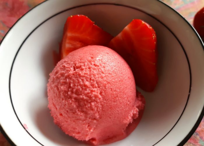 boule de sorbet rose dans un jatte avec deux quartiers de fraise