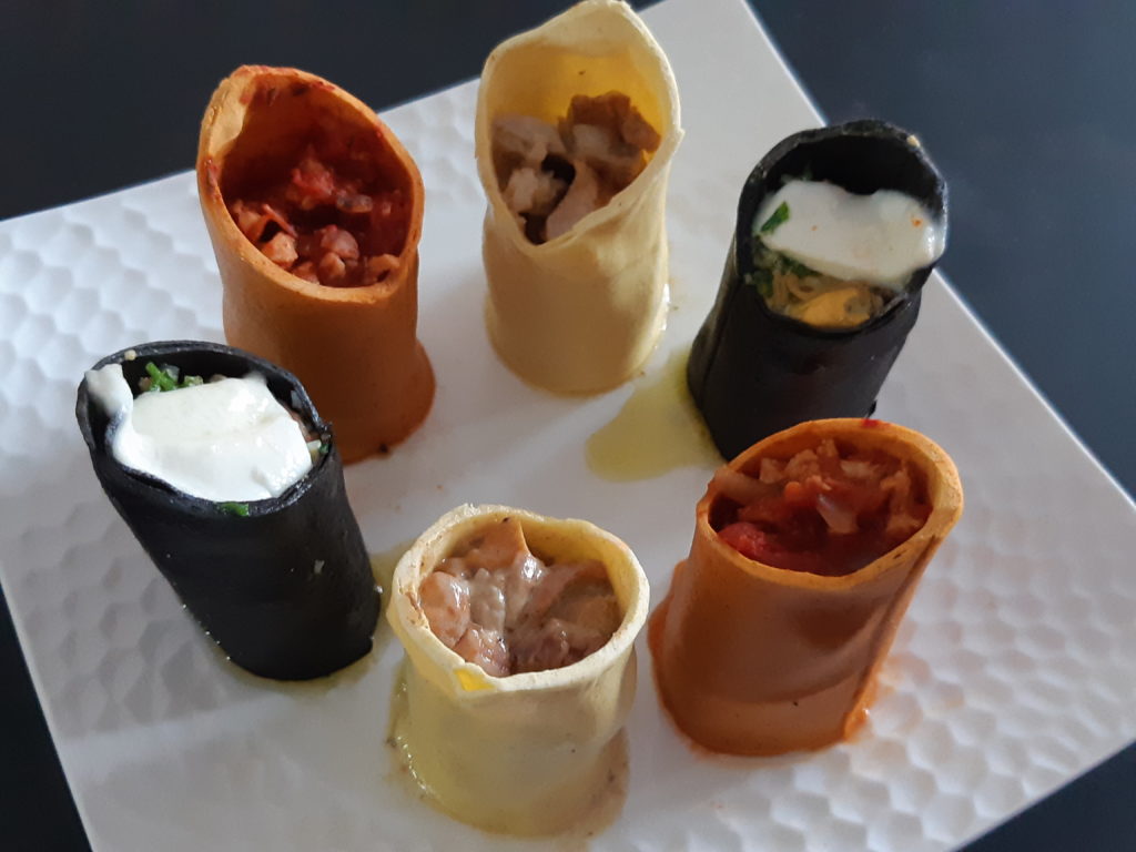 six cannelloni de trois couleurs différentes posés verticalement sur une assiette ils contiennent plusieurs préparations