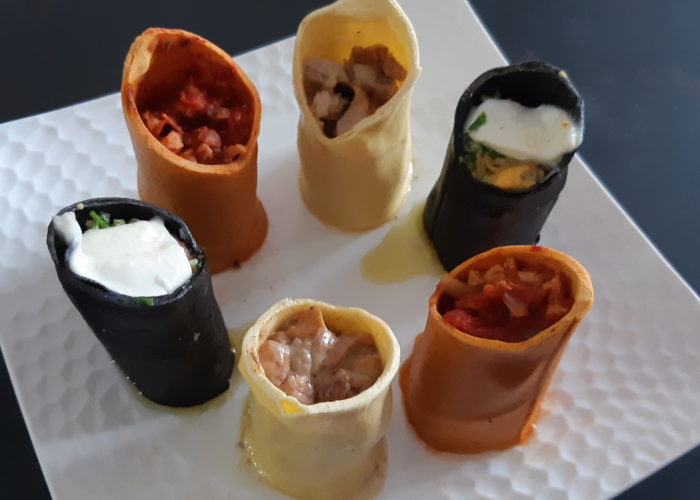 six cannelloni de trois couleurs différentes posés verticalement sur une assiette ils contiennent plusieurs préparations