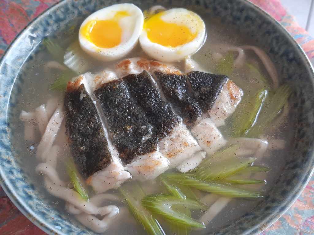 bol de ramen contenant des nouilles des légumes verts un filet de poisson tranché et un oeuf coupé en deux