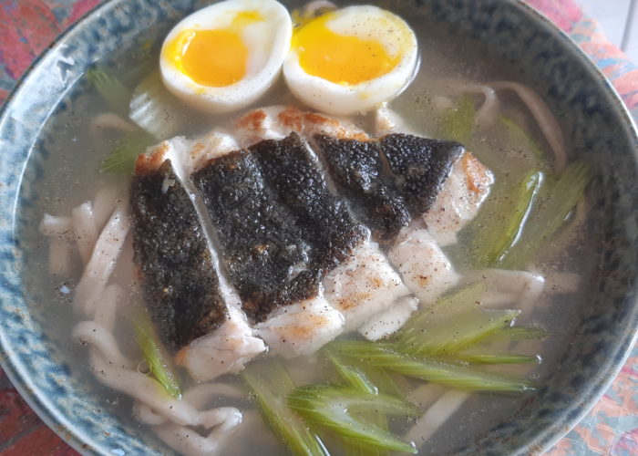 bol de ramen contenant des nouilles des légumes verts un filet de poisson tranché et un oeuf coupé en deux