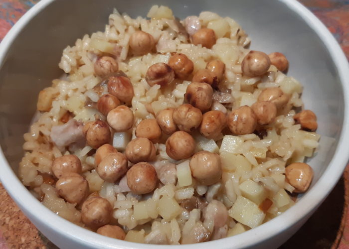 risotto contenant des légumes blancs et des morceaux de viande blanche recouvert de noisettes