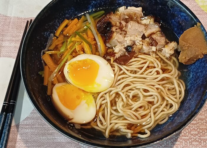 bol de ramen avec de la pâte miso su le bord droit on voit dans du bouillon clair des nouilles deux moities d'oeuf mollet du porc braisé et des legumes en julienne