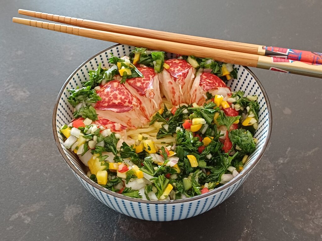 Queue de homard décortiquée avec de la verdure coupée fin dans un bol on voit des pates fines en dessous