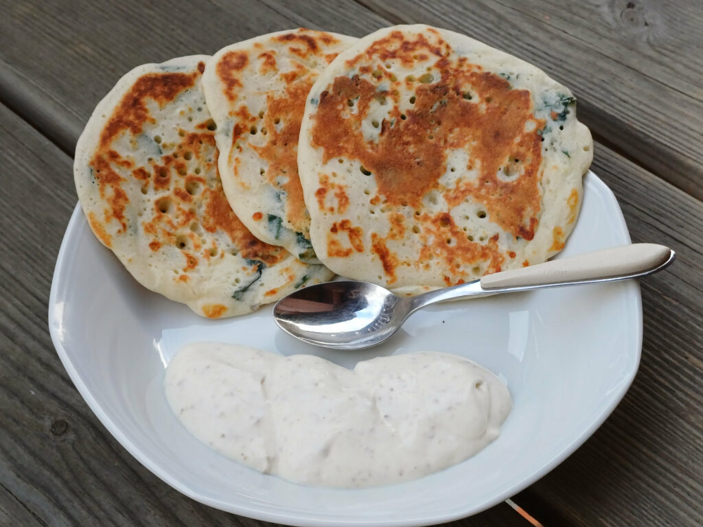 trois blinis larges en eventail sur le bord d'une assiette avec une sauce blanche