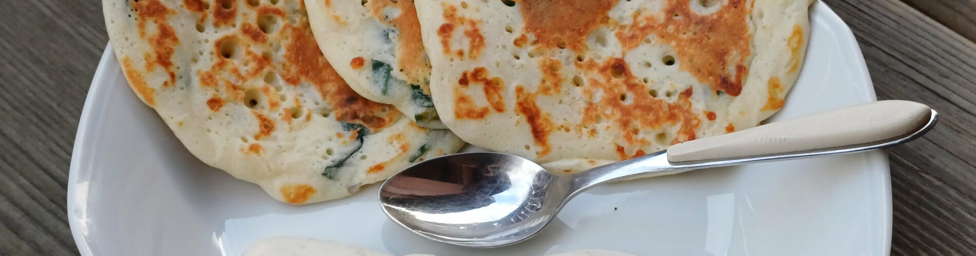 trois blinis larges en eventail sur le bord d'une assiette avec une sauce blanche