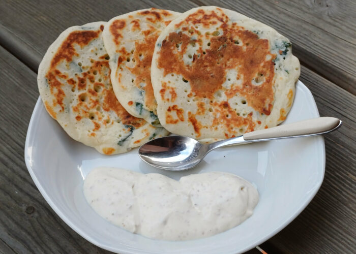 trois blinis larges en eventail sur le bord d'une assiette avec une sauce blanche